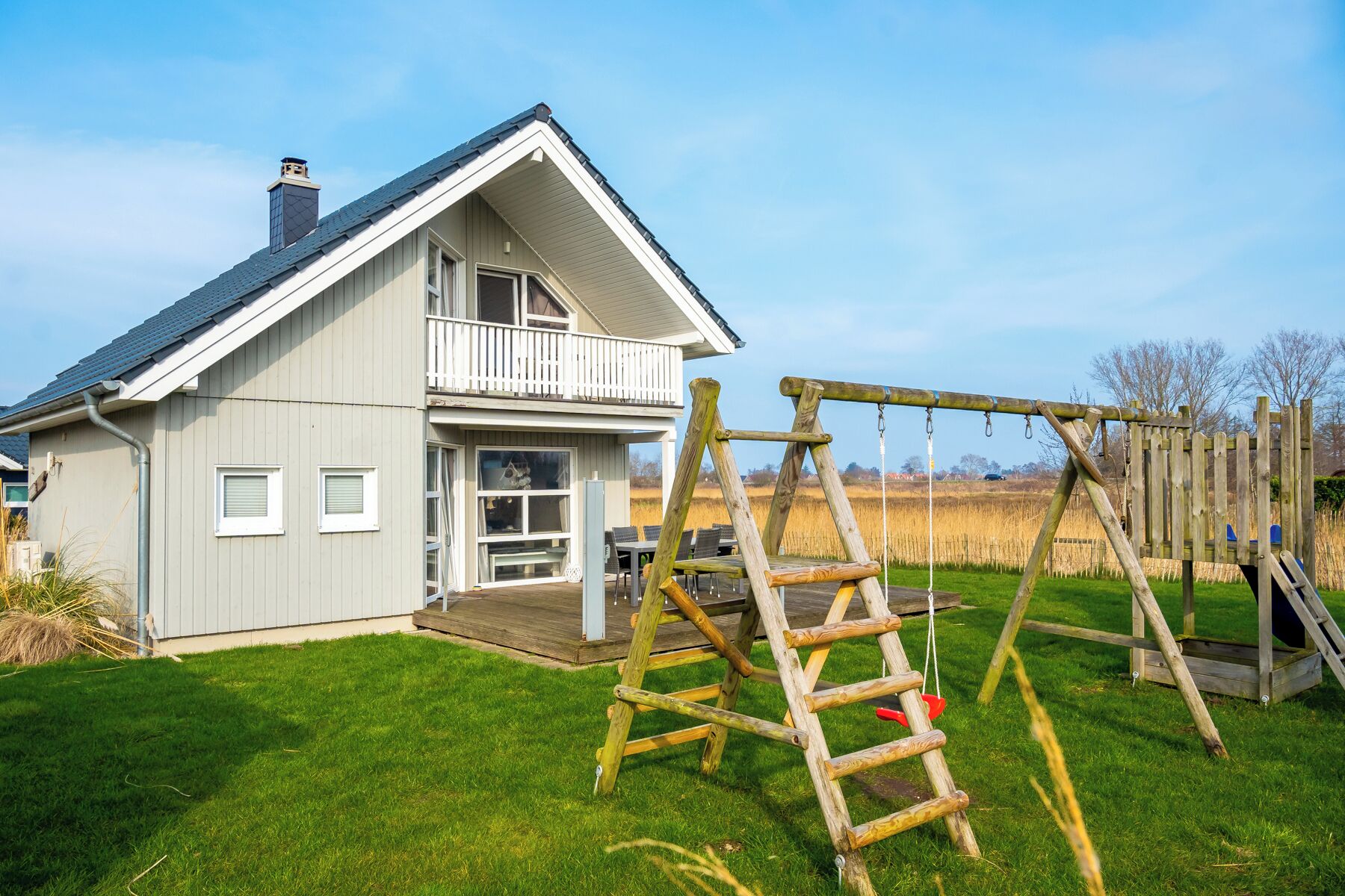 Et hus med skråtag, en balkon og et gyngestativ i gården.