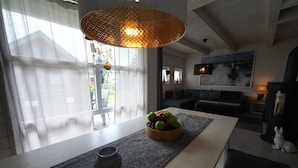 Ett modernt vardagsrum med ett stort fönster, ett träbord med frukt, en grå matta och en hängande lampa.