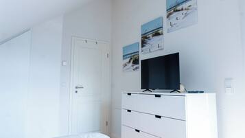 A bedroom with a bed, a white dresser with drawers, a flat-screen TV, and three framed pictures on the wall.