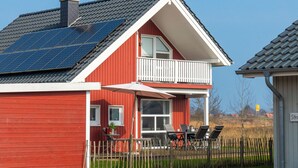 A red house with a balcony, solar panels, and a fenced outdoor seating area. - Ferienhaus "Plüschmors" in Schönberg-Holm: Sauna, Kamin, 600 m Strand, Strandkor (Schönberg (Holstein))