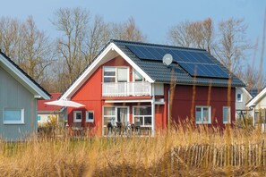 Et rødt hus med balkon, solpaneler på taget og en hvid parasol foran.