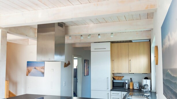 A modern kitchen with a black countertop, stainless steel appliances, and wooden cabinets. - Ferienhaus "Plüschmors" in Schönberg-Holm: Sauna, Kamin, 600 m Strand, Strandkor (Schönberg (Holstein))