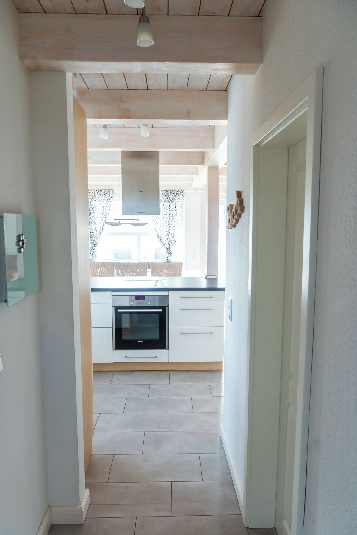 Eine Küche mit weißen Schränken, einem eingebauten Backofen und einem Fenster mit gemusterten Vorhängen.