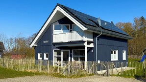 A two-story house with a balcony, solar panels, and a fenced yard. - Family Holiday Home with Sauna near the Sandy Beach in Schönberg-Holm (Schönberg (Holstein))
