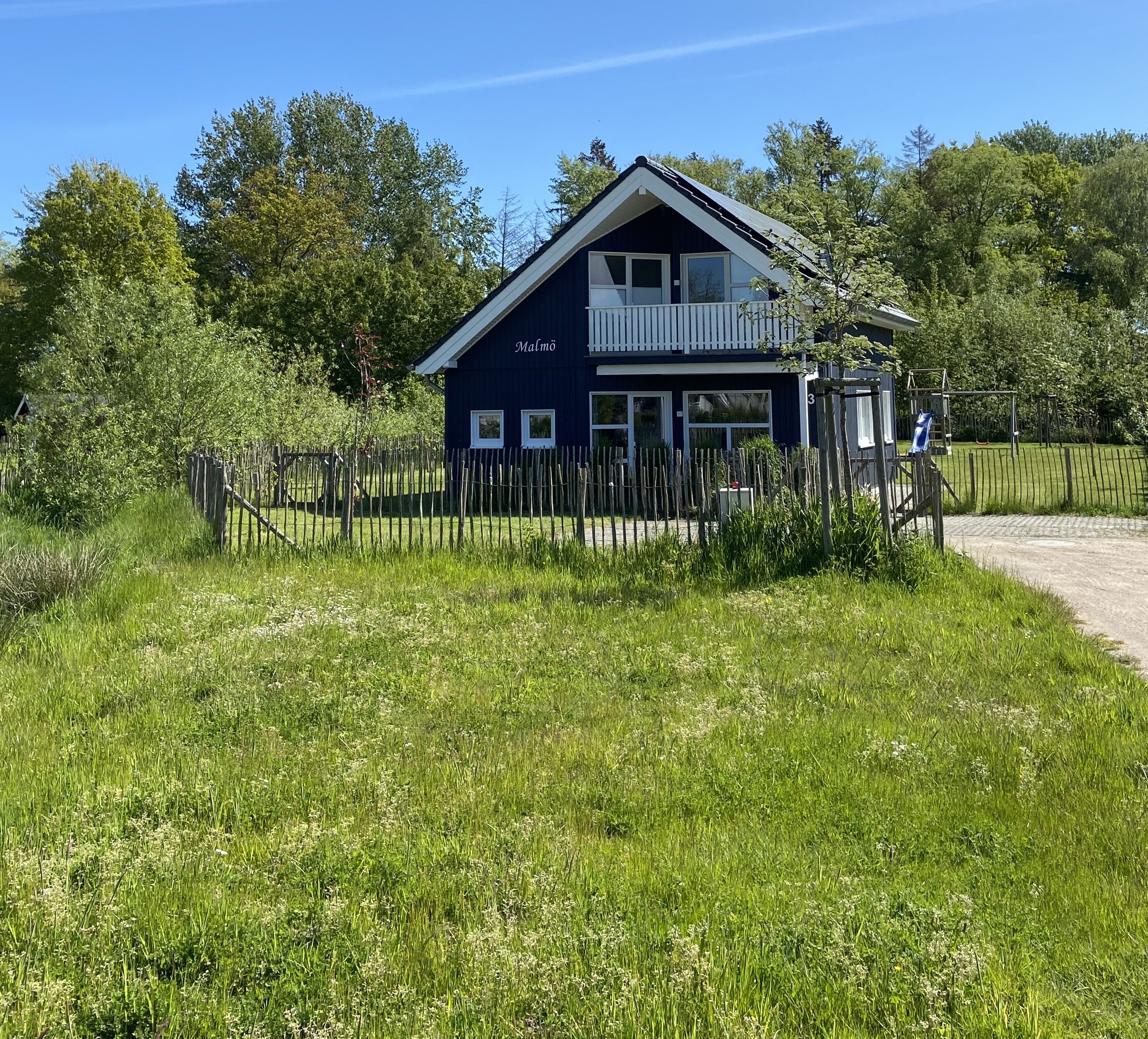 Een gebouw met twee verdiepingen en een balkon, omgeven door een houten hek en weelderige beplanting.