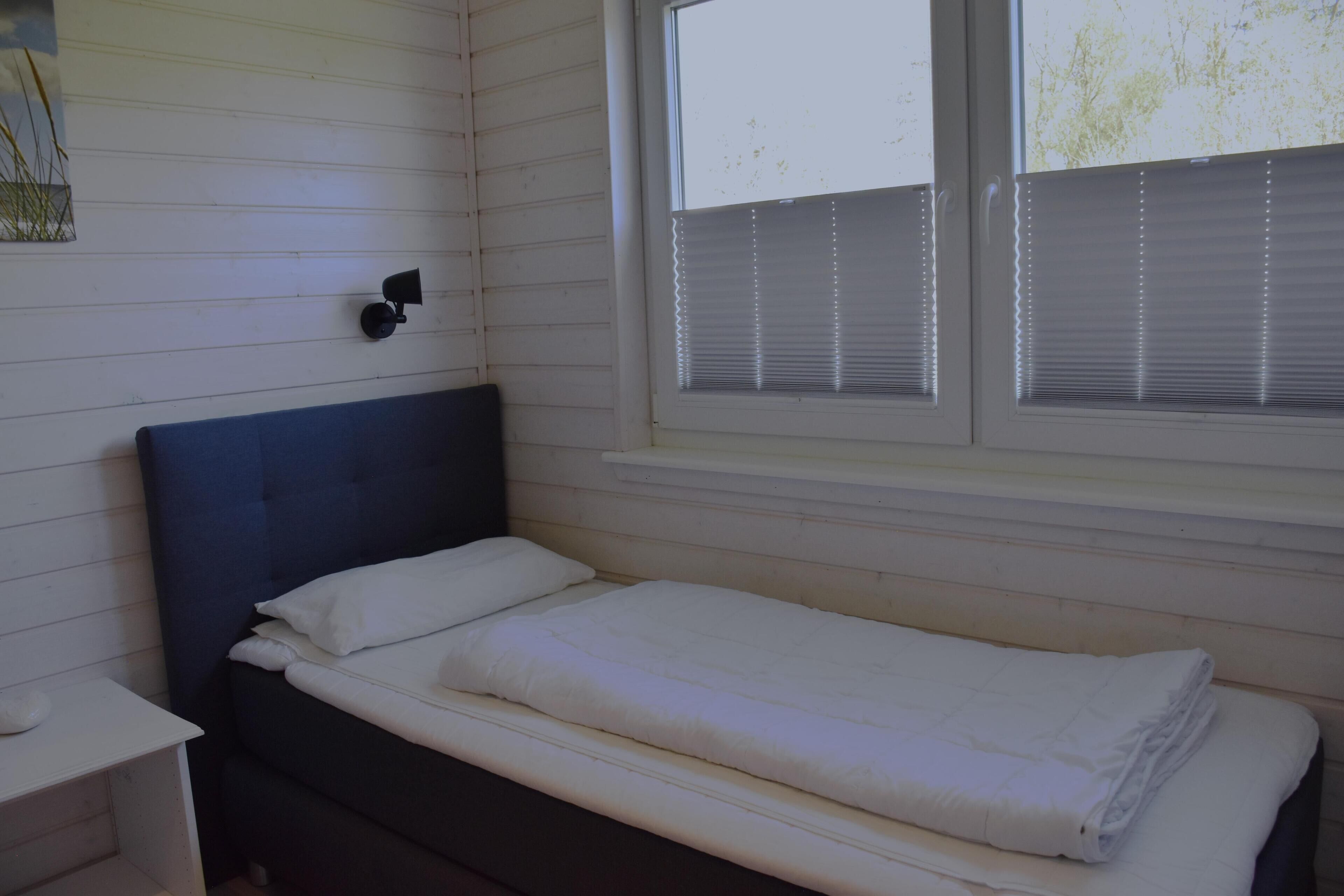 A single bed with a headboard, a bedside table, and a window with blinds.
