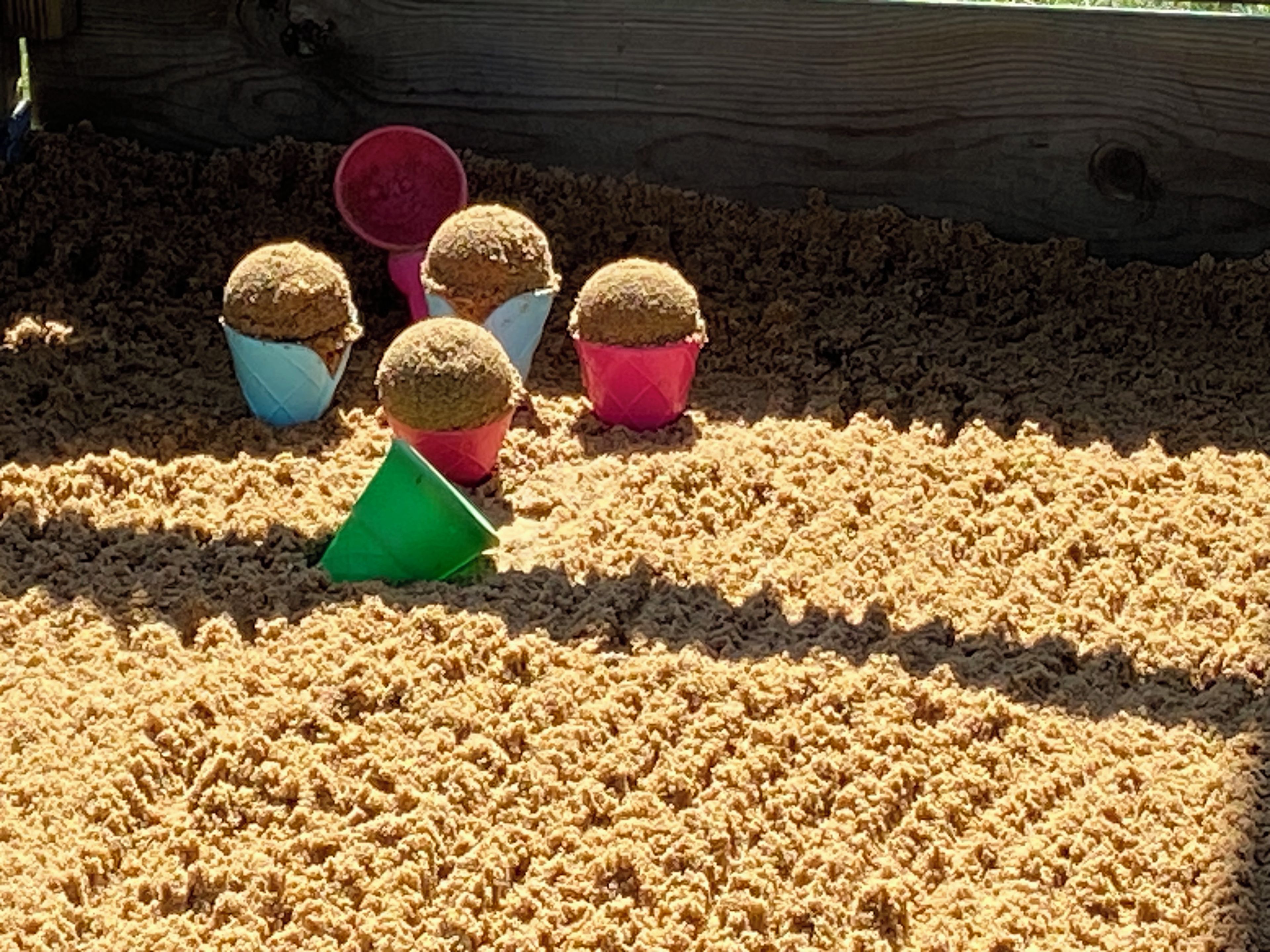 A sandbox with four sand molds and a green shovel.