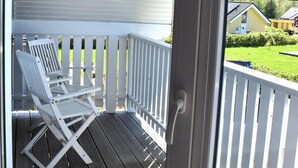 A wooden deck with two white chairs, a white railing, and a view of a house through a window. - Family Holiday Home with Sauna near the Sandy Beach in Schönberg-Holm (Schönberg (Holstein))