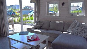A room with a sofa, a table with a remote control, and a view of the outside. - Family Holiday Home with Sauna near the Sandy Beach in Schönberg-Holm (Schönberg (Holstein))