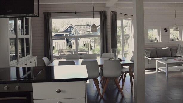 A modern kitchen with a TV, dining area with chairs, and a view of the outside. - Family Holiday Home with Sauna near the Sandy Beach in Schönberg-Holm (Schönberg (Holstein))