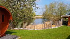 Eine Holzdiele mit umzäunter Terrasse, einem kleinen Teich und einem Rasenstück.