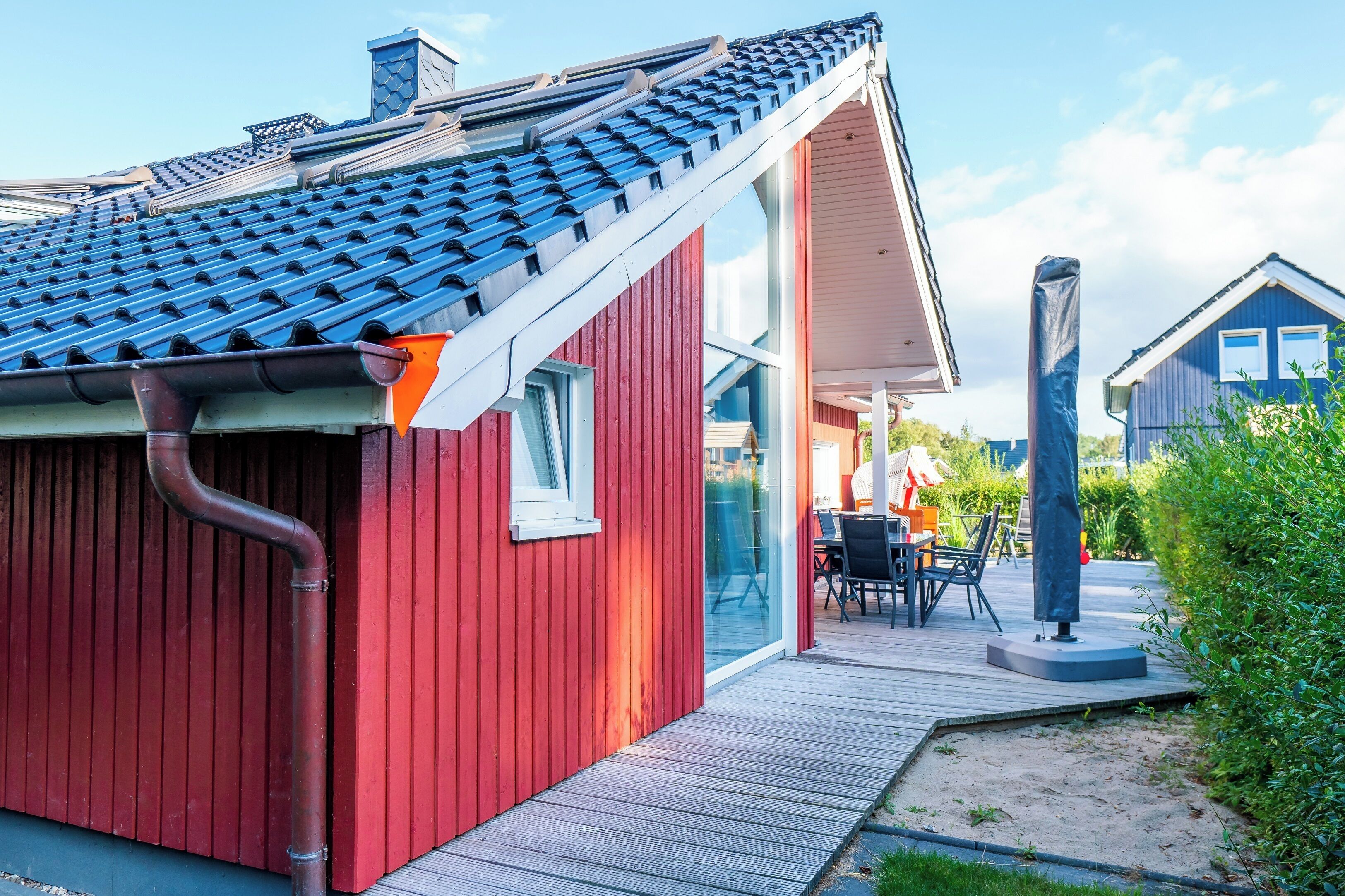 Ein rotes Gebäude mit einem geneigten Dach, einer Holzdielen-Terrasse und einer Glastür, die zu einem Außenbereich mit Sitzgelegenheiten führt.