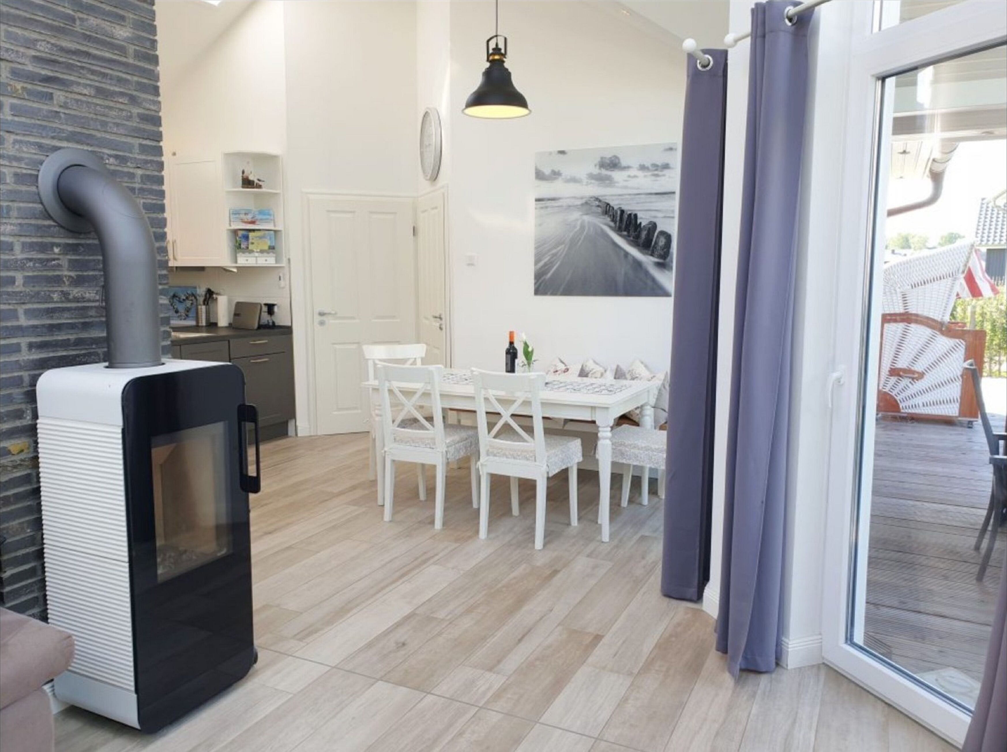 A modern kitchen with a built-in stove, a dining area with a white table and chairs, and a large window with a view of the outdoors.
