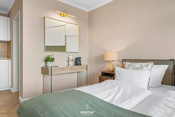 A hotel room with a bed, a bedside table with a lamp, a mirror, a small plant, and a wooden sideboard. - Ferienwohnung Margaritha in List auf Sylt mit Meerblick und direkt am Strand (List auf Sylt)