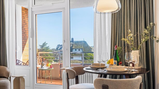 Ein Essbereich mit einem Tisch für zwei Personen, Blick auf einen Balkon und einer Weinflasche.