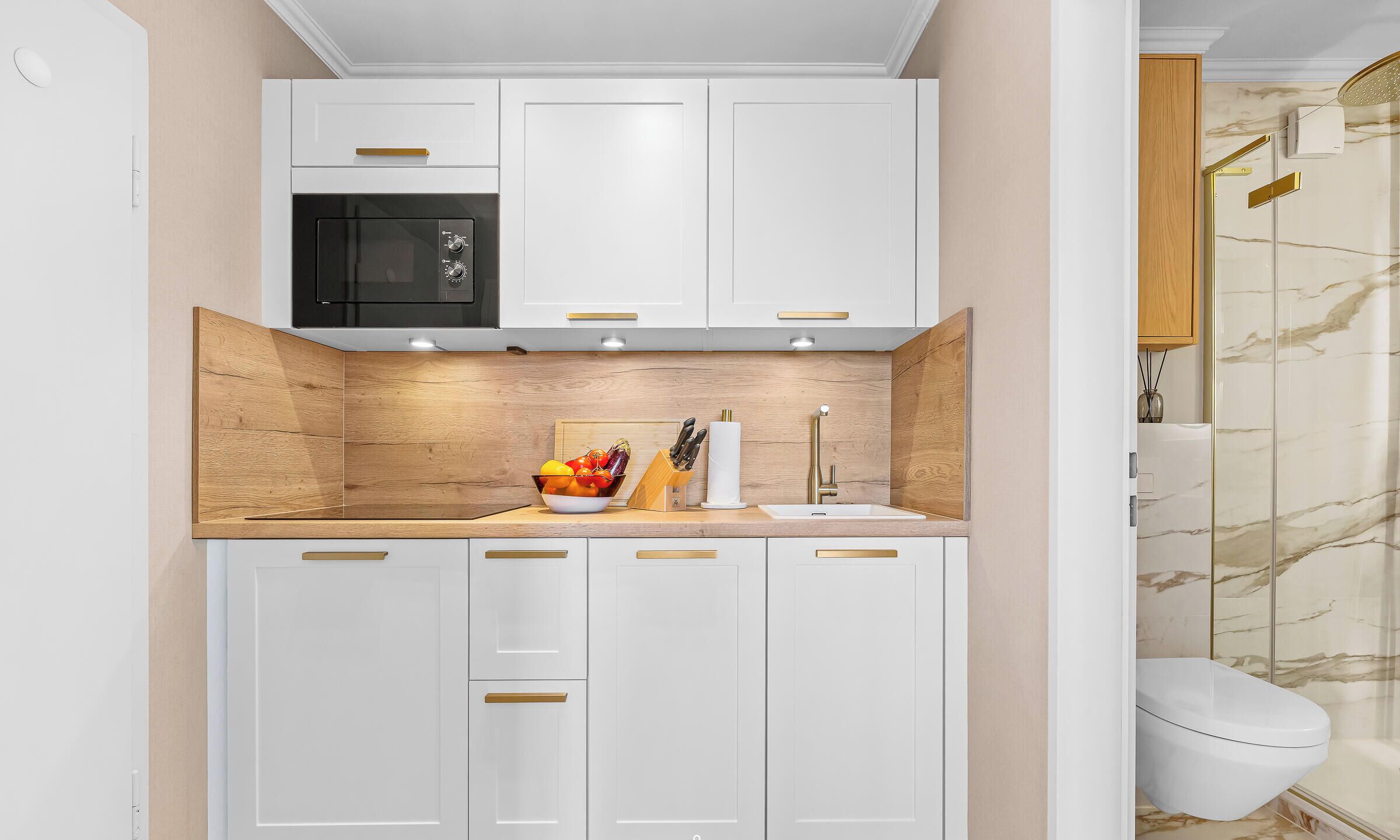 Una cocina moderna con armarios blancos, un microondas negro y un protector contra salpicaduras de madera.