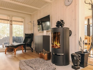 A cozy living room with a fireplace, a comfortable chair, a television, and a large window. - 4 Star Holiday Home in Lokken (Lokken)