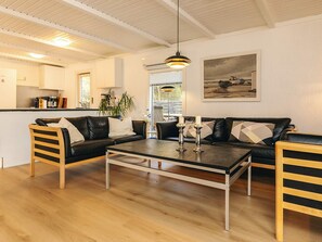 Ein modernes Wohnzimmer mit einem schwarzen Ledersofa, Holzstühlen, einem Glastisch und einem Gemälde an der Wand.