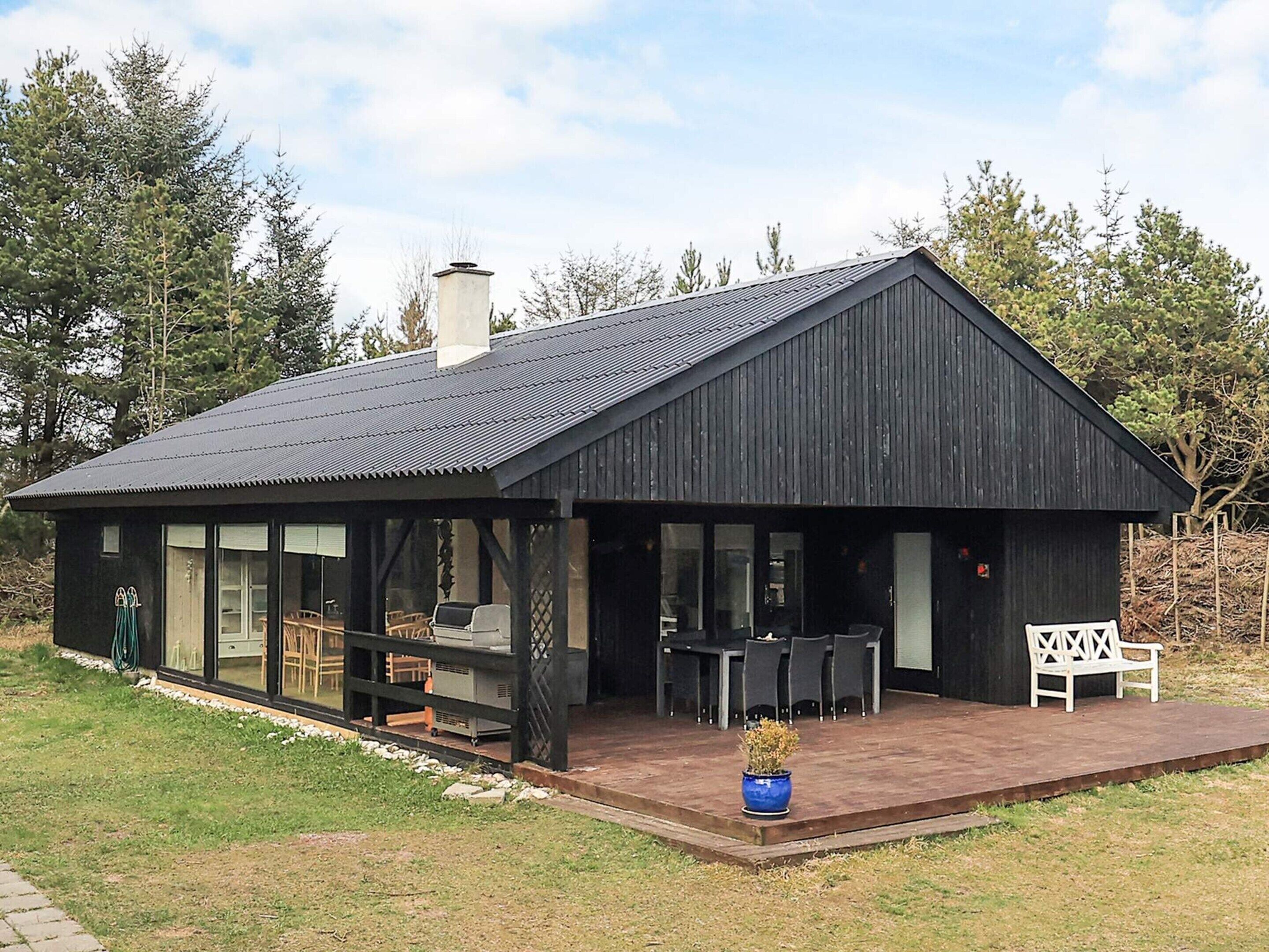 Een modern zwart huis met een groot terras, een barbecue en een bank.