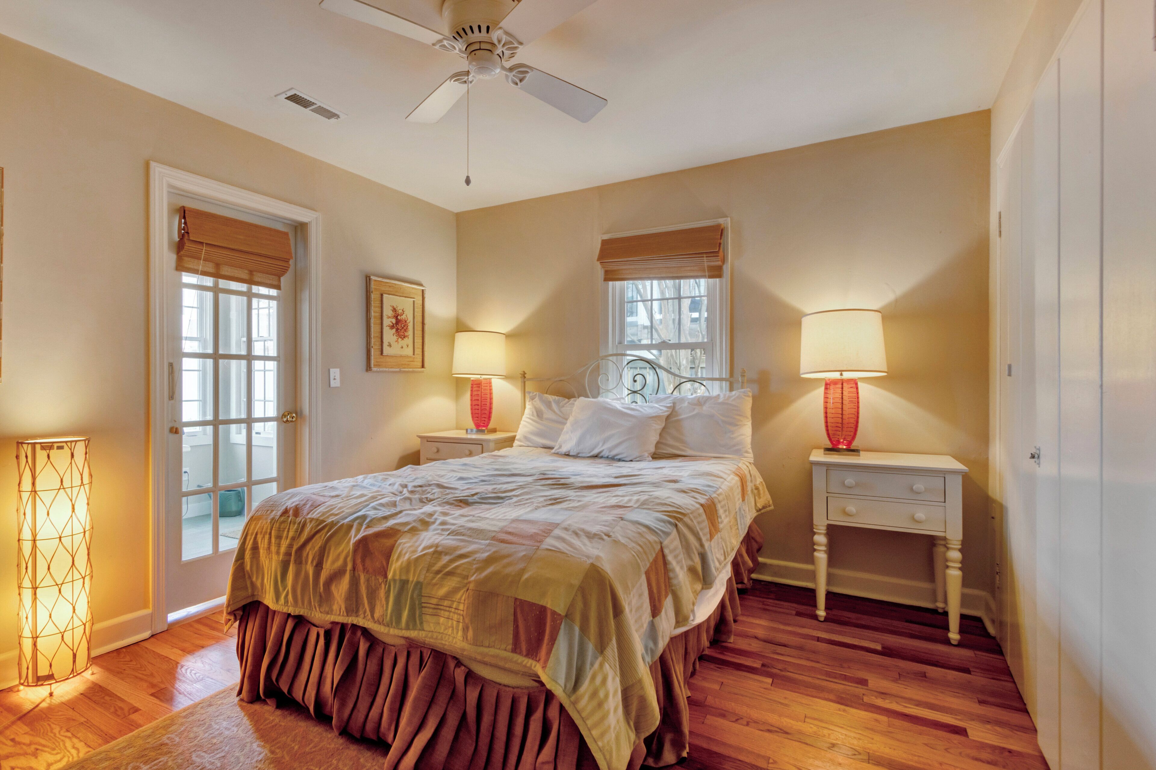 A bedroom with a bed, two bedside tables, a ceiling fan, and a window with blinds.