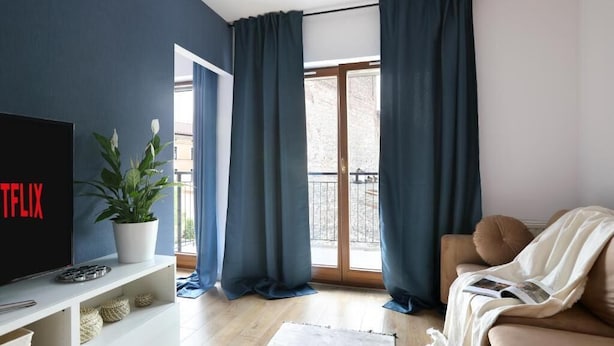 A living room with a TV, a plant, a sofa, and a balcony with curtains. - Malila Apartments City Center Pawia 34 (Kraków)