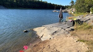 Une jetée au bord du lac, avec une chaise et un parasol, une eau claire et une rive rocheuse.