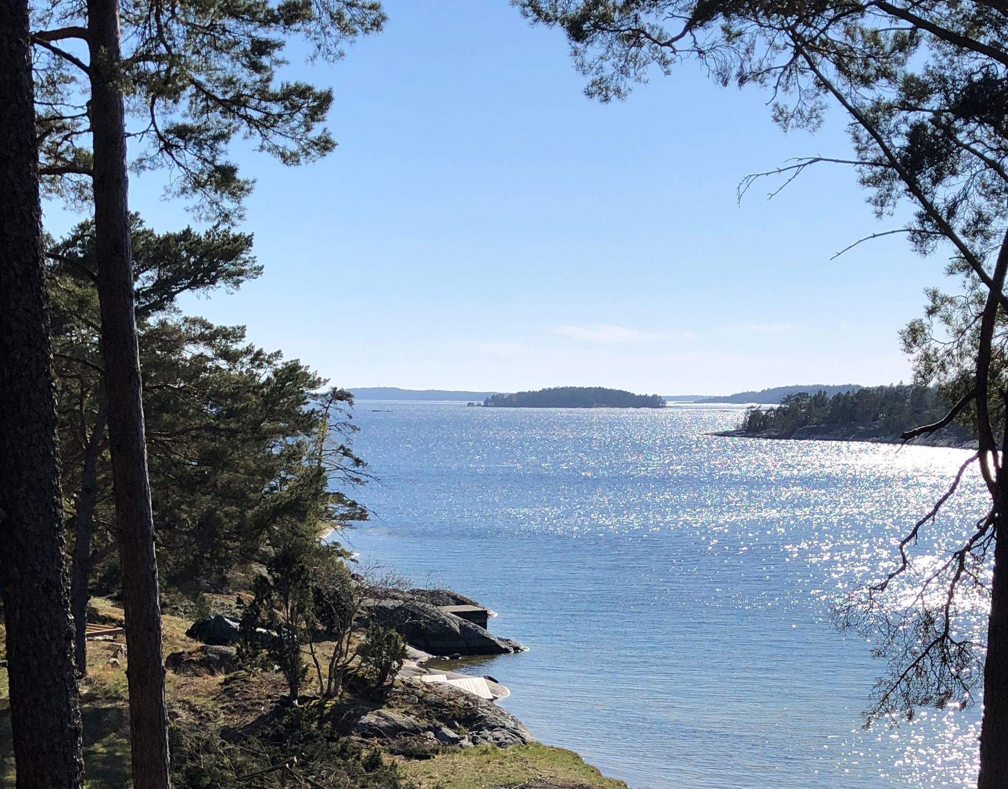 A coastal landscape with a clear view of the sea, surrounded by trees and rocky terrain.