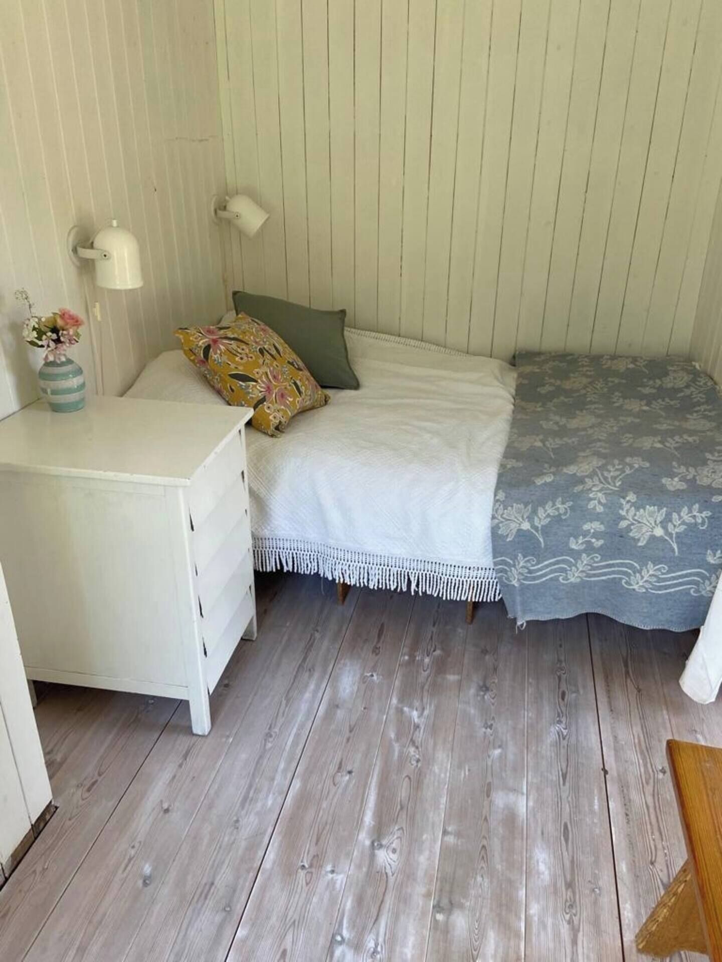 A small, cozy room with a bed, bedside table, lamp, and a decorative vase.