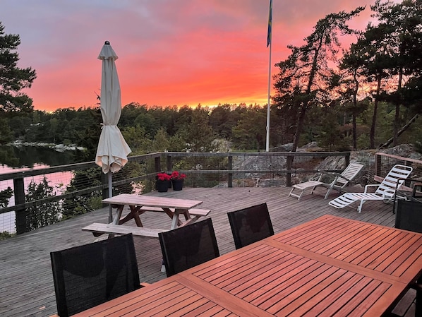 Puinen terassi, jossa on ulkokalusteita, lippu ja näkymä järvelle auringonlaskun aikaan.
