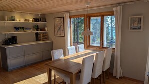 Une table à manger en bois avec des chaises, une cuisine avec des meubles gris et une grande fenêtre avec des rideaux.