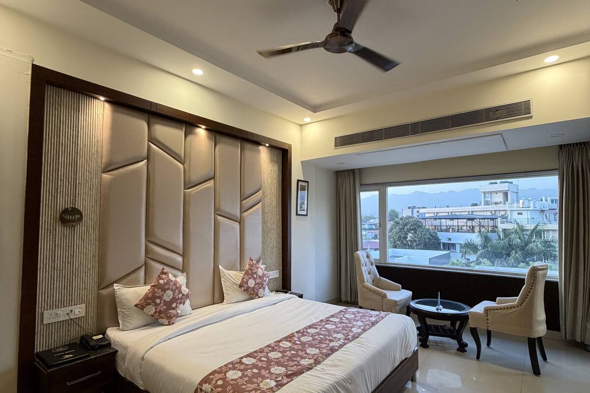 Habitación de hotel con una cama grande, un escritorio con silla, ventilador de techo y vistas a la ciudad.