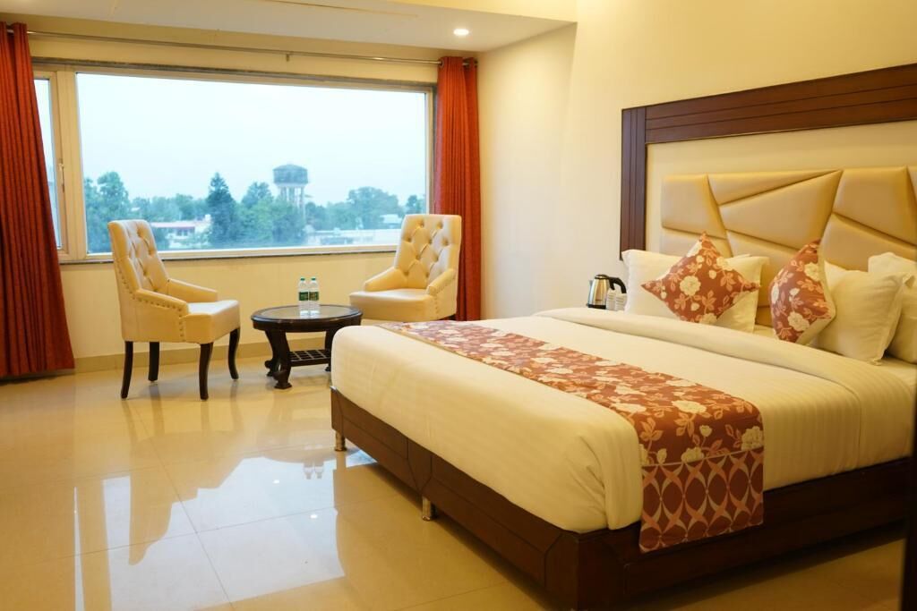 A hotel room with a large bed, two armchairs, a small table, and a view of trees through the window.
