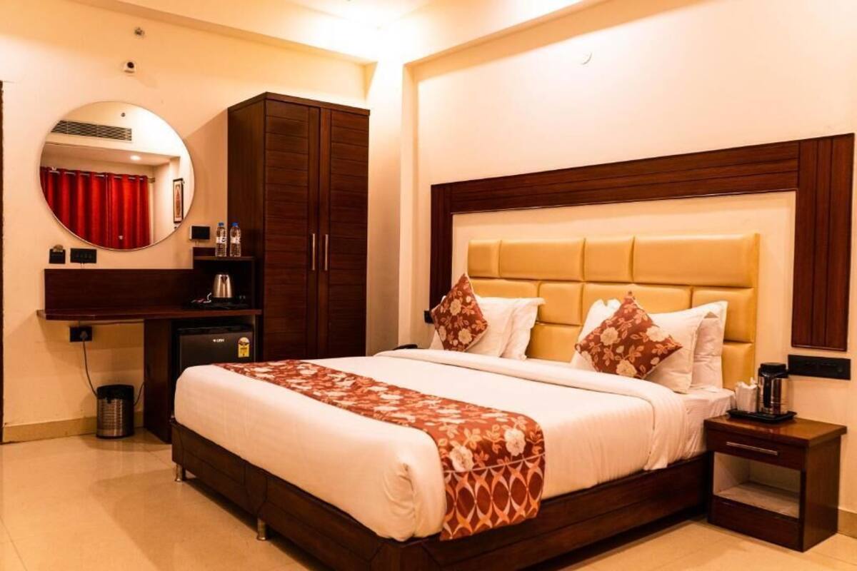 Habitación de hotel con una cama grande, un armario de madera, un escritorio con silla, un espejo redondo y un pequeño cubo de basura.