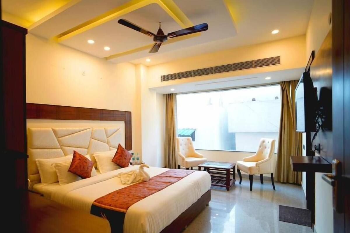 Habitación de hotel con una cama grande, ventilador de techo, televisión y balcón con sillas.