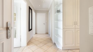 Un corridoio con una porta bianca, un quadro incorniciato appeso al muro e un armadietto bianco con ripiani.