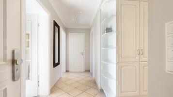 Un corridoio con una porta bianca, un quadro incorniciato appeso al muro e un armadietto bianco con ripiani.