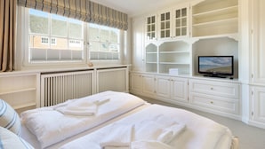 Camera d'albergo con due letti, televisore, finestra con persiane e armadio a muro con scaffali.