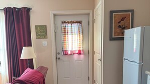 Une pièce comprenant un lit, une lampe, un réfrigérateur, une porte avec un rideau et un mur orné d’un tableau.