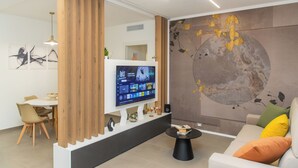 A modern living room with a flat-screen TV, a sofa with cushions, a coffee table, and a dining area with chairs and a table. - Suite 20five, Romantic Suite with In-Room Jacuzzi Hot Tub. (Bari)