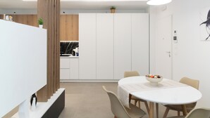 A modern kitchen with white cabinets, a wooden accent wall, and a dining area with a white table and chairs. - Suite 20five, Romantic Suite with In-Room Jacuzzi Hot Tub. (Bari)