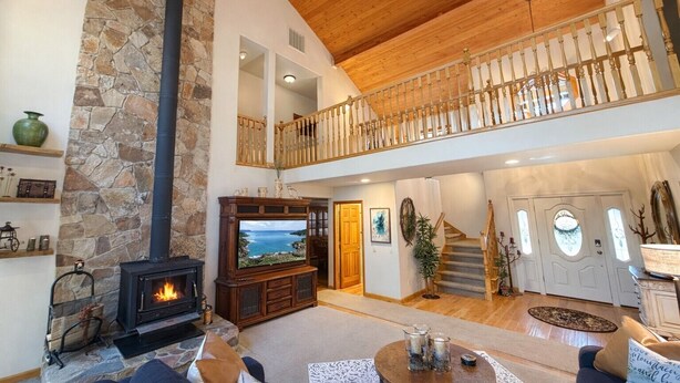 Un amplio salón con chimenea de piedra, un televisor grande y una escalera de madera que sube a un nivel superior.