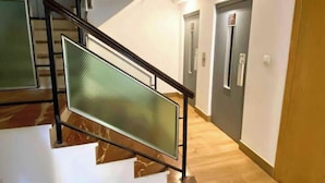 En trappe med glasgelænder, trægulv og en dør med et skilt for elevator.