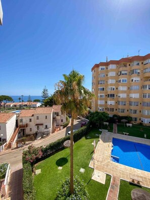 A residential area with a swimming pool, a palm tree, and a multi-story building with balconies. - Apartment With Sea Views in Mijas Costa (Mijas)