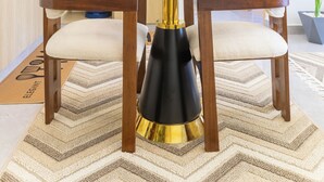 Eine moderne Küche mit weißen Schränken, einem Esstisch mit Stühlen, einer schwarz-goldenen Standleuchte und einem Blumentopf.