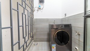Ein kompakter Waschraum mit integriertem Wasch- und Trockner, einer an der Wand montierten Steuerung und einer Maschendrahttür.