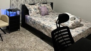 Une chambre à coucher comprenant un lit, un bureau, une chaise, une commode et une fenêtre avec des rideaux à motifs.