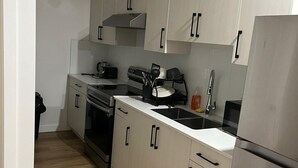 Une cuisine moderne avec des meubles blancs, des appareils en acier inoxydable et un parquet en bois disposé en motif chevrons.