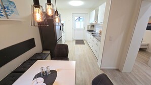 A modern kitchen with white cabinets, a dining area with a table and chairs, and pendant lighting. - Beachfront vacation apartment "Ostseebrise" in Wendtorf with fenced garden - Hun (Wendtorf)