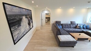 A modern living room with a large ocean-themed artwork, a grey sectional sofa, and a wooden coffee table. - Beachfront vacation apartment "Ostseebrise" in Wendtorf with fenced garden - Hun (Wendtorf)