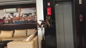 Een hotellobby met een beige bank, een muurschildering van een stadsgezicht, een lift en een potplant.